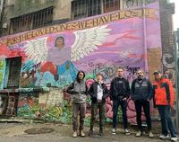 A group of people standing in front of a mural that reads 'For the loved ones we have lost'