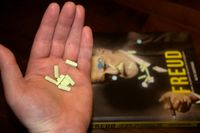 Une main est représentée tenant une poignée de pilules.